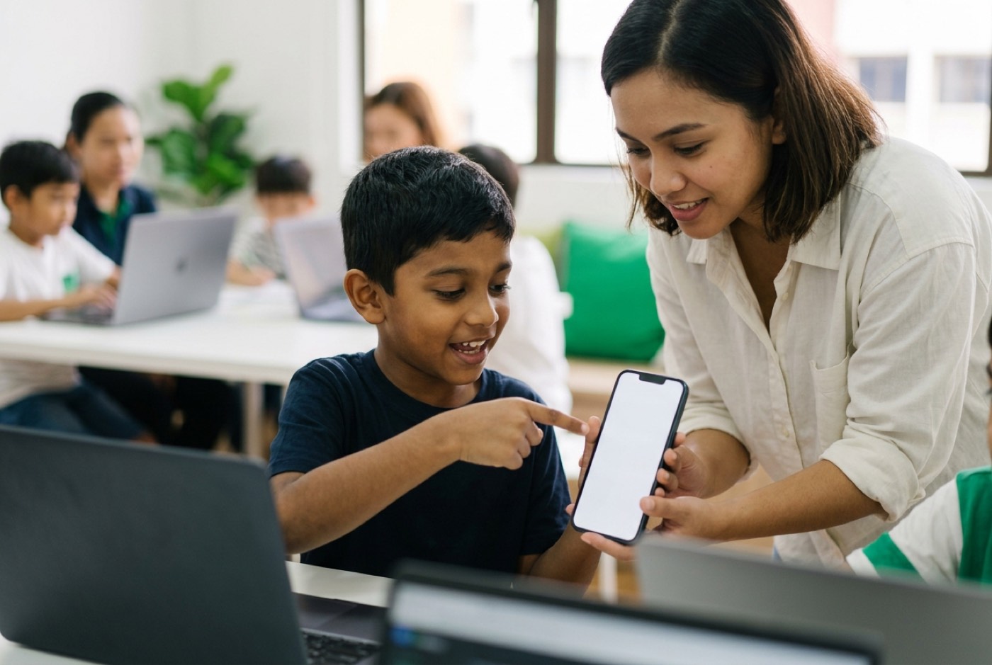 A primary school child pointing excitedly at an app prototype displayed on a phone while an instructor guides them