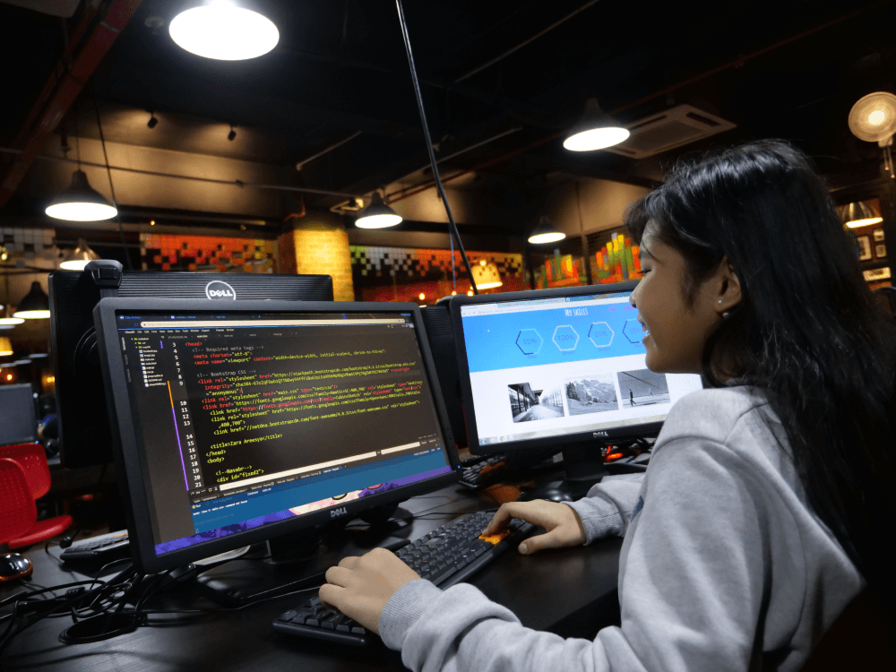 Girl coding HTML and CSS on dual monitors